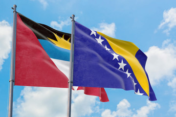 Bosnia Herzegovina and Antigua and Barbuda flags waving in the wind against white cloudy blue sky together. Diplomacy concept, international relations.