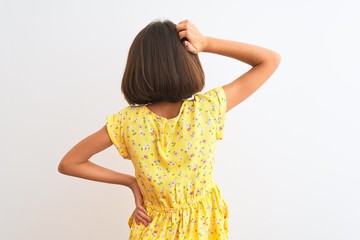 Young beautiful child girl wearing yellow floral dress standing over isolated white background Backwards thinking about doubt with hand on head