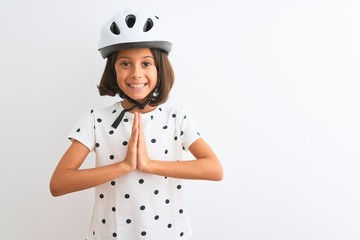Beautiful child girl wearing security bike helmet standing over isolated white background praying with hands together asking for forgiveness smiling confident.