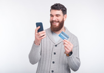 Ready to buy online and checking my balance on web banking. Young man is holding his phone and credit card on white background.