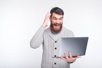 What great news. Surprised young man is holding his laptop and looking at it shocked.