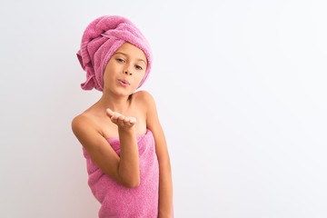 Beautiful child girl wearing shower towel after bath standing over isolated white background looking at the camera blowing a kiss with hand on air being lovely and sexy. Love expression.