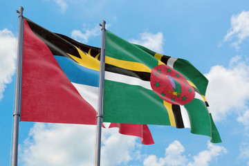 Dominica and Antigua and Barbuda flags waving in the wind against white cloudy blue sky together. Diplomacy concept, international relations.