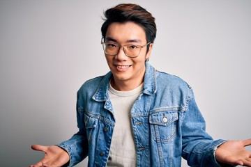 Young handsome chinese man wearing denim jacket and glasses over white background clueless and...