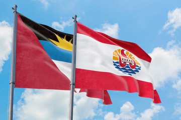 French Polynesia and Antigua and Barbuda flags waving in the wind against white cloudy blue sky together. Diplomacy concept, international relations.