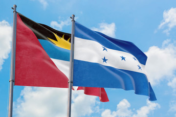 Honduras and Antigua and Barbuda flags waving in the wind against white cloudy blue sky together. Diplomacy concept, international relations.