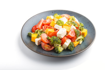 Vegetarian salad with broccoli, tomatoes, feta cheese, and pumpkin on a blue ceramic plate isolated on white background, side view.
