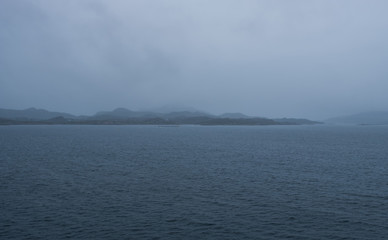 One of the car ferries between Mortavika and Arsvagen sailing in harsh sea with some big waves and mountain ridge landscape in the background, Norway
