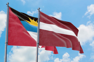 Latvia and Antigua and Barbuda flags waving in the wind against white cloudy blue sky together. Diplomacy concept, international relations.
