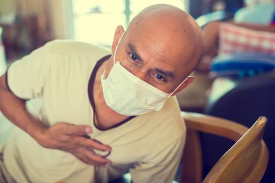 Scenario Of An Asian Man Fell Ill At Home With A Corona Virus. He Was Requesting Help. Bald Asian Man Wearing A Mask To Protect Against Viruses.