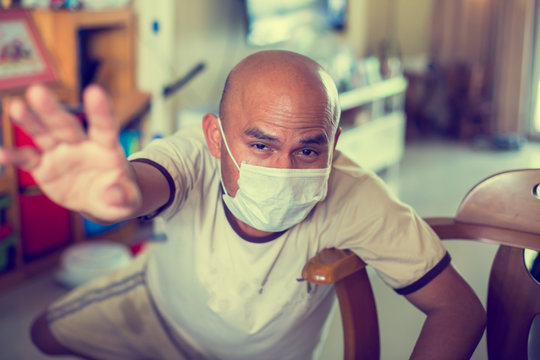 Scenario Of An Asian Man Fell Ill At Home With A Corona Virus. He Was Requesting Help. Bald Asian Man Wearing A Mask To Protect Against Viruses.