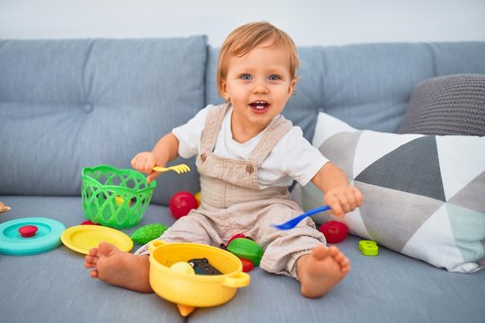 Adorable blonde toddler smiling happy sitting on the sofa playing with plastic meals toys at home