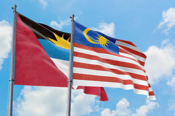 Malaysia and Antigua and Barbuda flags waving in the wind against white cloudy blue sky together. Diplomacy concept, international relations.