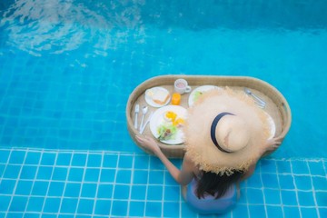 Portrait young asian woman happy smile enjoy with floating breakfast tray in swimming pool in hotel