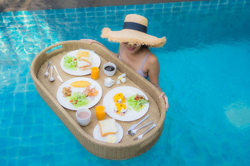 Portrait young asian woman happy smile enjoy with floating breakfast tray in swimming pool in hotel