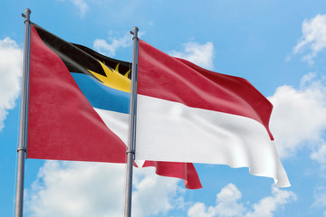 Monaco and Antigua and Barbuda flags waving in the wind against white cloudy blue sky together. Diplomacy concept, international relations.