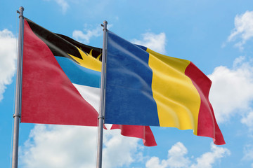 Romania and Antigua and Barbuda flags waving in the wind against white cloudy blue sky together. Diplomacy concept, international relations.