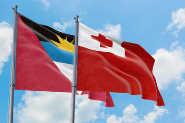 Tonga and Antigua and Barbuda flags waving in the wind against white cloudy blue sky together. Diplomacy concept, international relations.