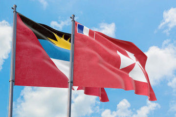 Wallis And Futuna and Antigua and Barbuda flags waving in the wind against white cloudy blue sky together. Diplomacy concept, international relations.