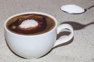 A cup of coffee with a hill of sugar and a spoon