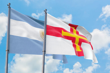 Guernsey and Argentina flags waving in the wind against white cloudy blue sky together. Diplomacy concept, international relations.