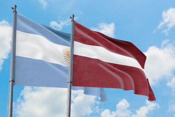 Latvia and Argentina flags waving in the wind against white cloudy blue sky together. Diplomacy concept, international relations.