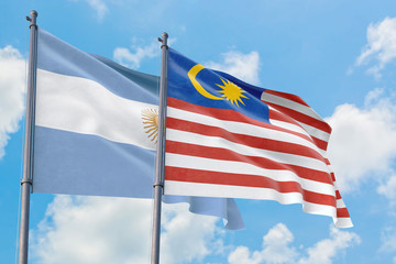 Malaysia and Argentina flags waving in the wind against white cloudy blue sky together. Diplomacy concept, international relations.