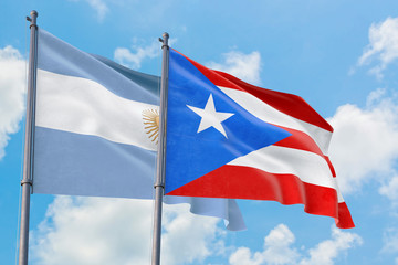 Puerto Rico and Argentina flags waving in the wind against white cloudy blue sky together. Diplomacy concept, international relations.