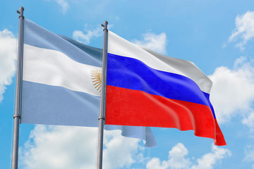 Russia and Argentina flags waving in the wind against white cloudy blue sky together. Diplomacy concept, international relations.