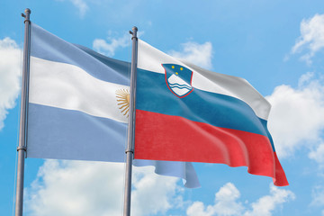 Slovenia and Argentina flags waving in the wind against white cloudy blue sky together. Diplomacy concept, international relations.