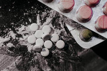 scattered white small tablets on a scattered white powder on a black flat background top view macro