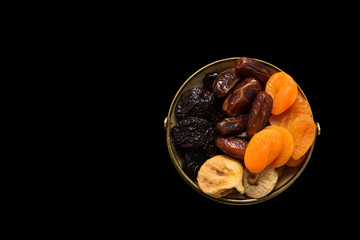 Mix of  dried fruits in wooden bowl on dark wood background. View from above.