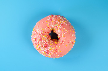 Pink iced donut on blue background. Sweet dessert top view .