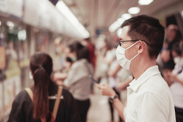 Asian man wearing glasses and medical face mask waiting for public train with crowd,  coronavirus, covid-19 delta virus post pandemic, air pollution and health, new normal, reopening concept