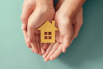 Hands holding yellow paper house on blue background, family home, homeless shelter housing and home protecting insurance, mortgage concept, foster home care, family day care