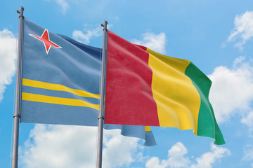 Guinea and Aruba flags waving in the wind against white cloudy blue sky together. Diplomacy concept, international relations.