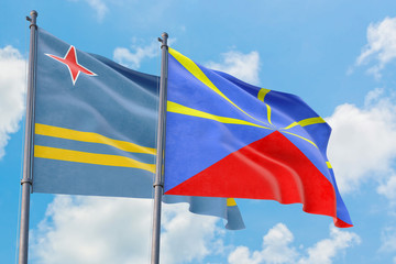 Reunion and Aruba flags waving in the wind against white cloudy blue sky together. Diplomacy concept, international relations.