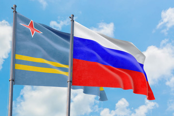 Russia and Aruba flags waving in the wind against white cloudy blue sky together. Diplomacy concept, international relations.
