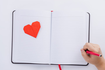 The female hand is holding a pen and red heart shapes on the notebook over the white background....