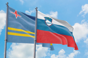 Slovenia and Aruba flags waving in the wind against white cloudy blue sky together. Diplomacy concept, international relations.