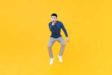 Fototapeta na wymiar Asian man jumping in mid-air doing pointing gesture