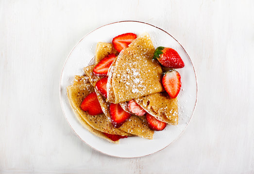 Crepes with strawberries on white background, top view.