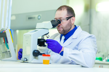 Naklejka na ściany i meble Laboratory worker performing urinalysis using microscope and laboratory equipment in a medical laboratory