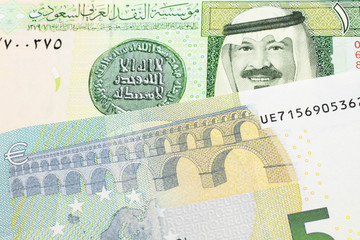 A green one riyal bank note from Saudi Arabia with a blue and green five euro bank note close up in macro
