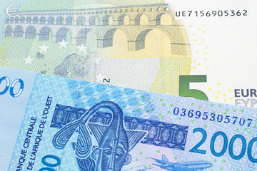 A close up image of a blue, West African franc bank note with a five Euro bank note in macro