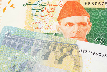 An orange and green twenty Pakistani rupee bank note with a red one hundfive Euro bank note in macro