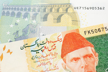 An orange and green twenty Pakistani rupee bank note with a red one hundfive Euro bank note in macro