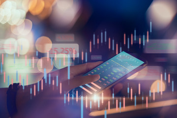 Stock exchange market concept, hand trader touching on smartphone with graphs analysis candle line on bokeh colors light in night atmospheric city.