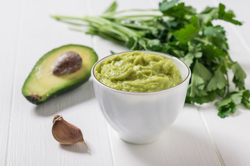 Guacamole in a white porcelain Cup on a wooden table. Diet vegetarian Mexican food avocado.