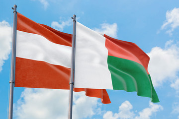 Madagascar and Austria flags waving in the wind against white cloudy blue sky together. Diplomacy concept, international relations.